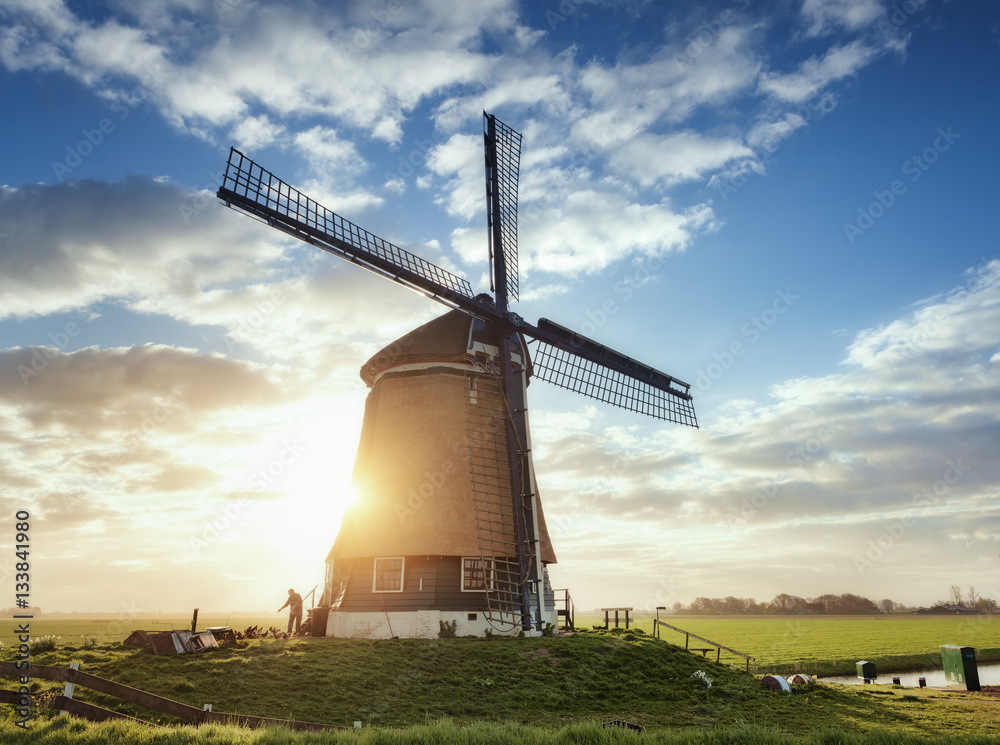 Windmill and silhouette of a man at sunrise in Netherlands. Beautiful old dutch windmill against col