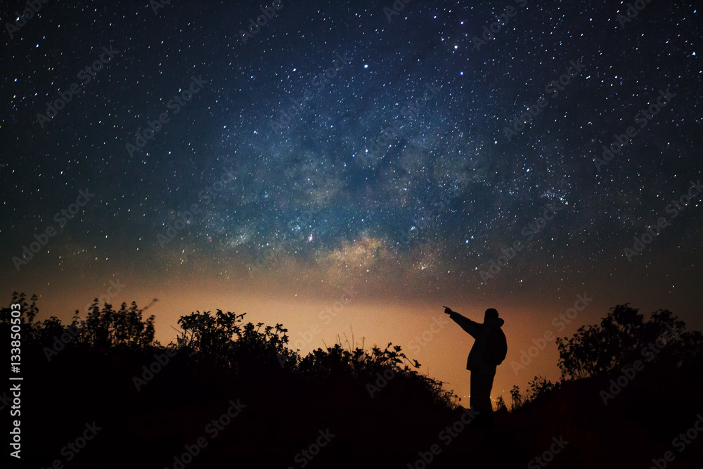 A Man is standing next to the milky way galaxy pointing on a bri