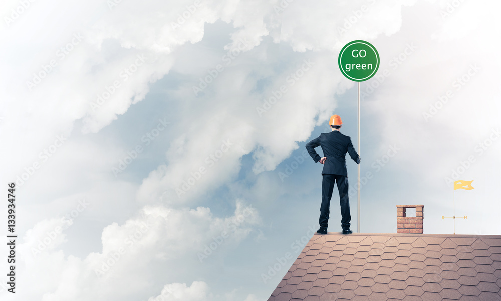 Businessman in suit on house top with ecology concept signboard.