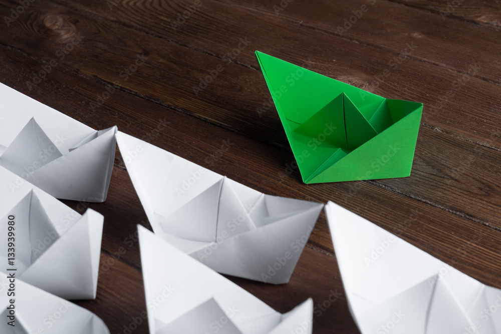 Business leadership concept with white and color paper boats on wooden table