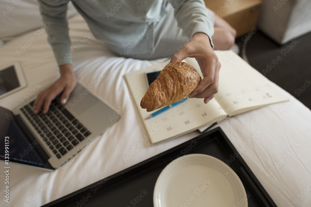 The woman is eating a simple breakfast while working at the hotel