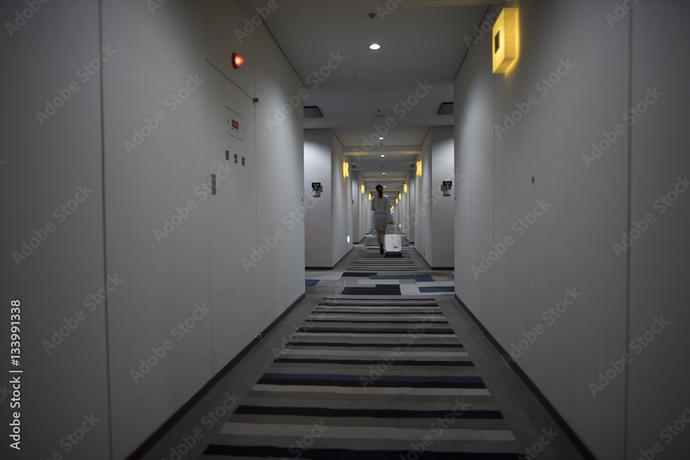 The woman is walking in the hotel corridor with a suitcase