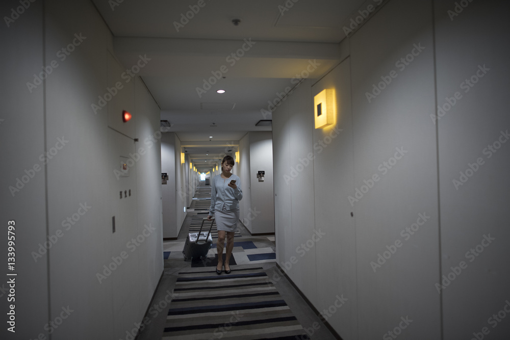 The woman is walking in the hotel corridor with a suitcase