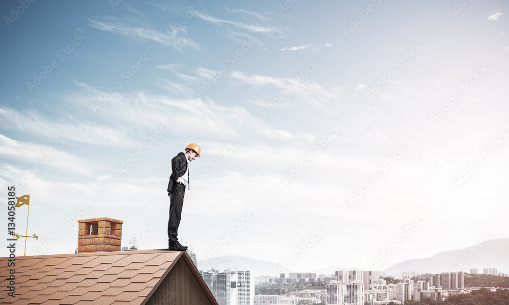 Businessman looking down from roof and modern cityscape at backg