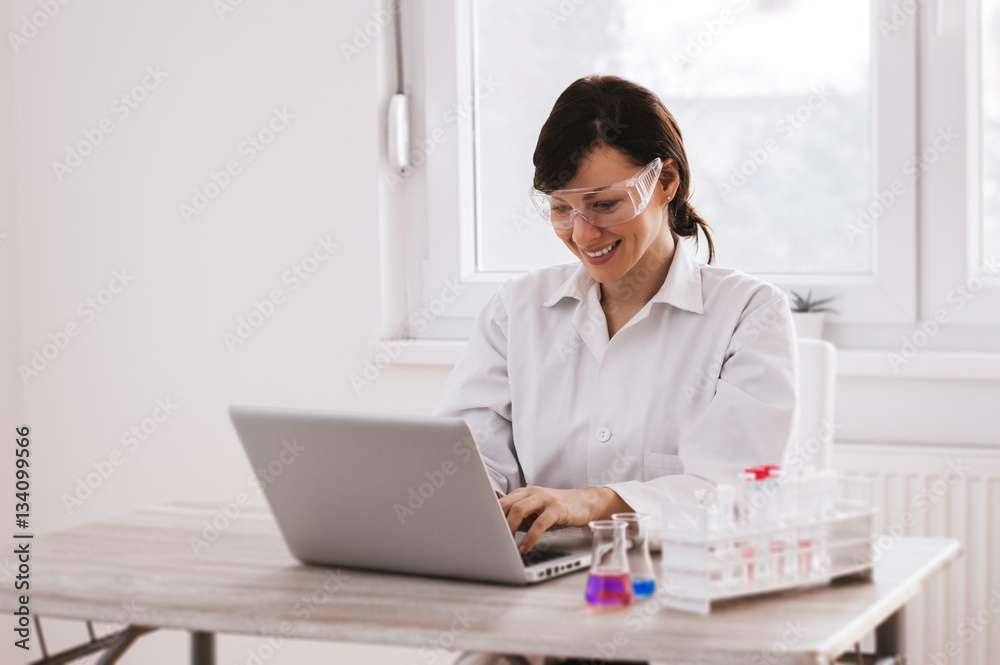 Scientist working with chemicals and typing on laptop in the lab