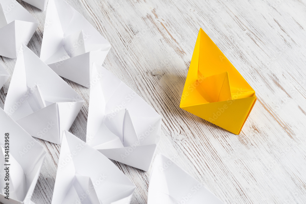 Business leadership concept with white and color paper boats on wooden table