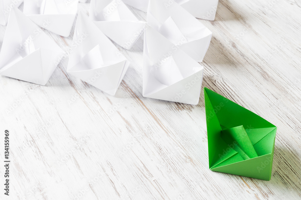 Business leadership concept with white and color paper boats on wooden table