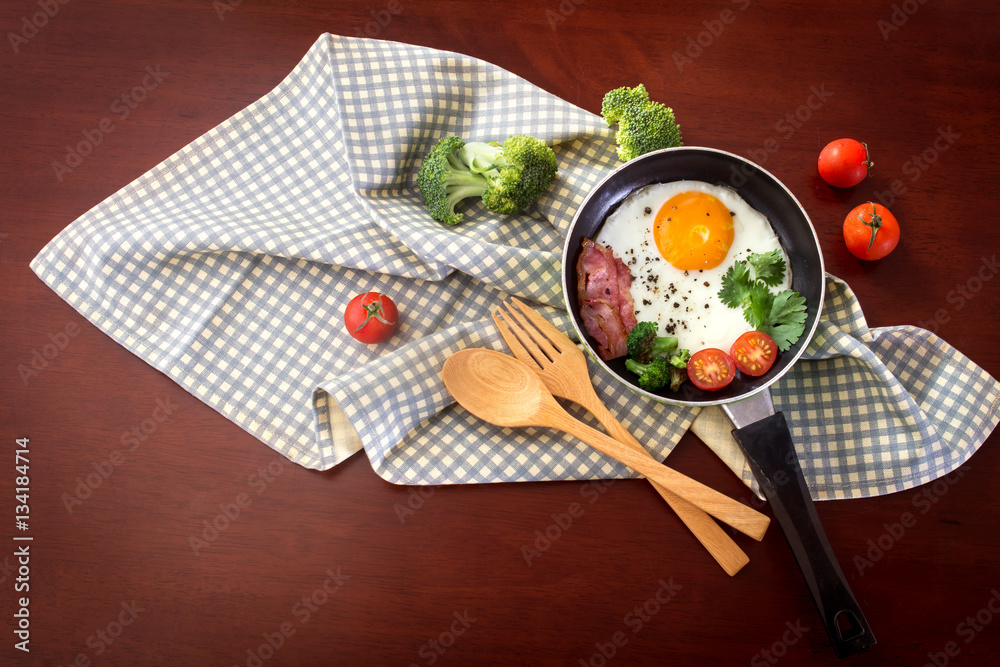 Breakfast with fried egg and bacon in dark pan on the table