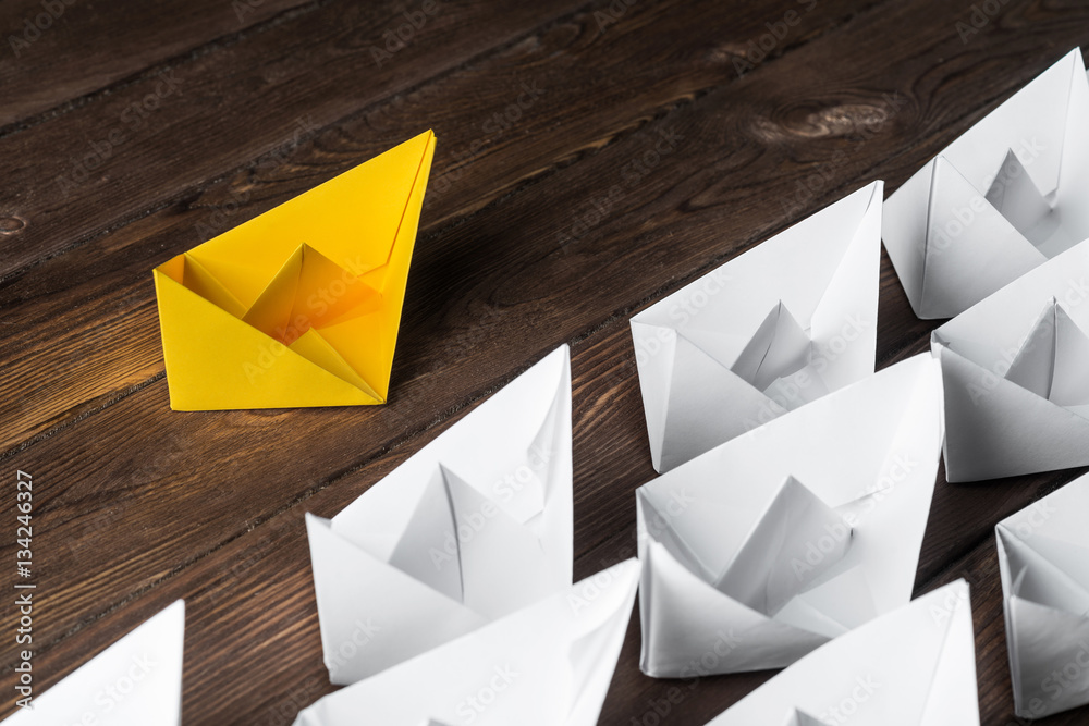 Business leadership concept with white and color paper boats on wooden table