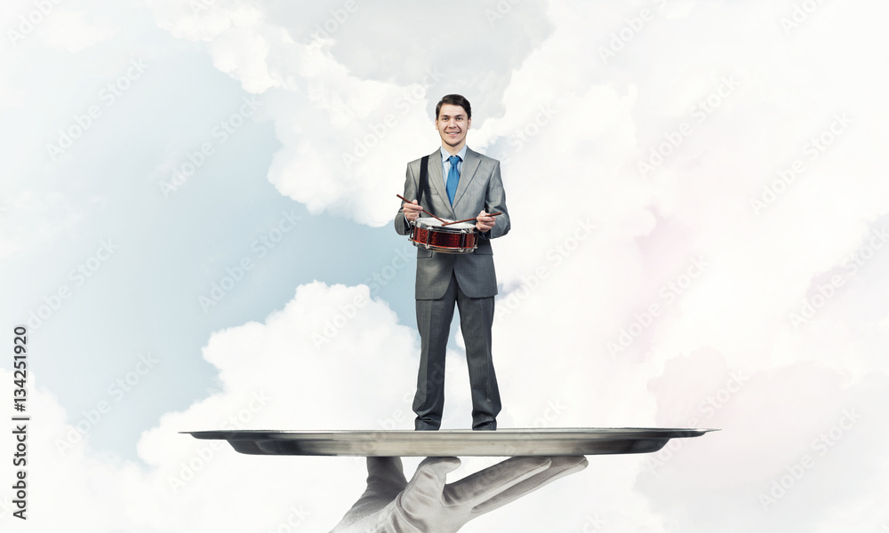 Businessman on metal tray playing drum blue sky background