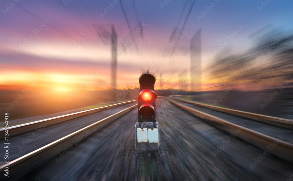 Railway station and semaphore with motion blur effect against colorful sky with clouds at sunset. Co