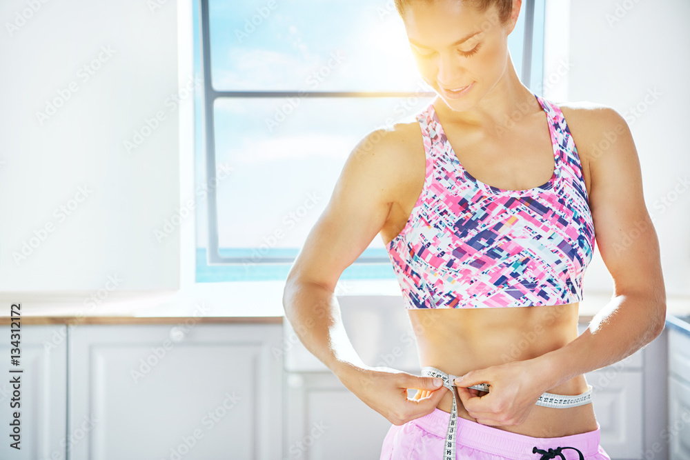 Woman in sunlight measuring waistline with tape