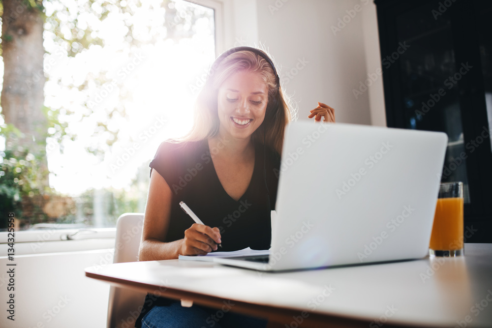 Happy young woman studying in kitchen