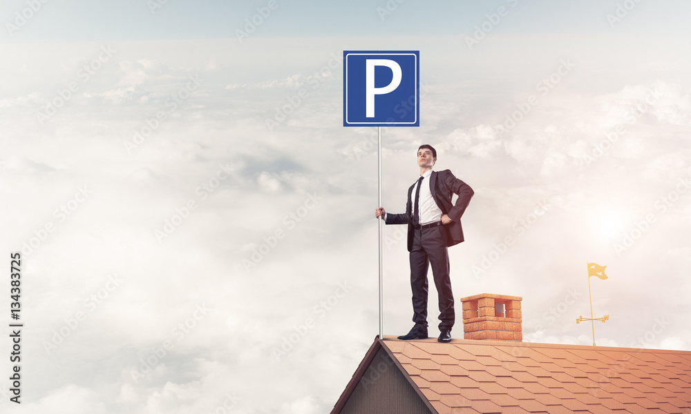 Young businessman with parking sign standing on brick roof. Mixe