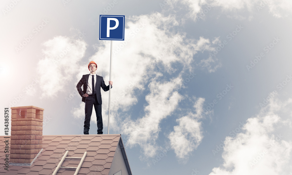 Young businessman with parking sign standing on brick roof. Mixe