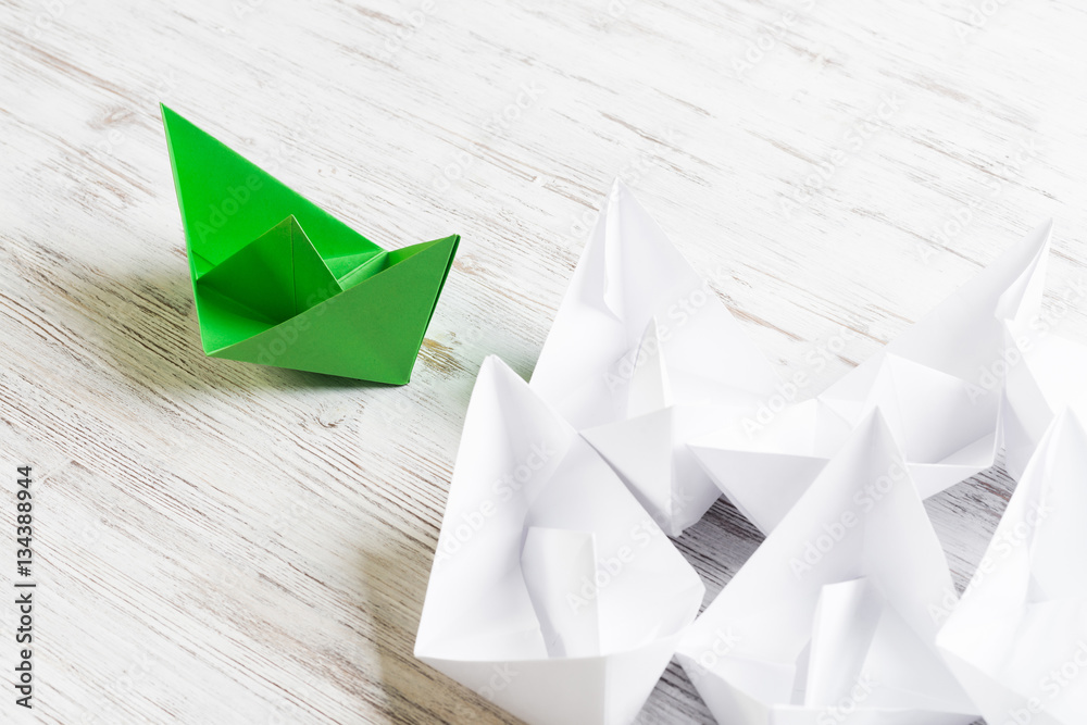 Business leadership concept with white and color paper boats on wooden table