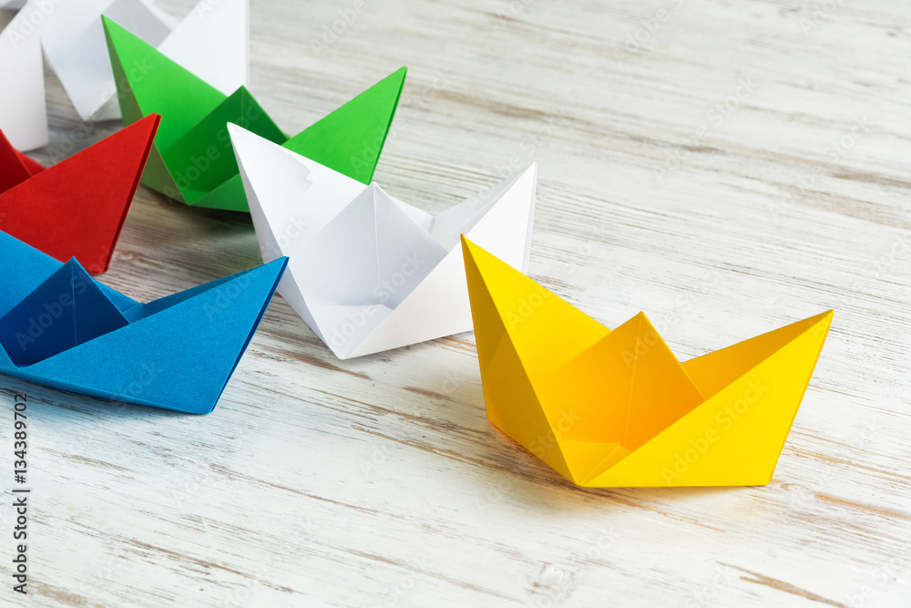 Business leadership concept with white and color paper boats on wooden table