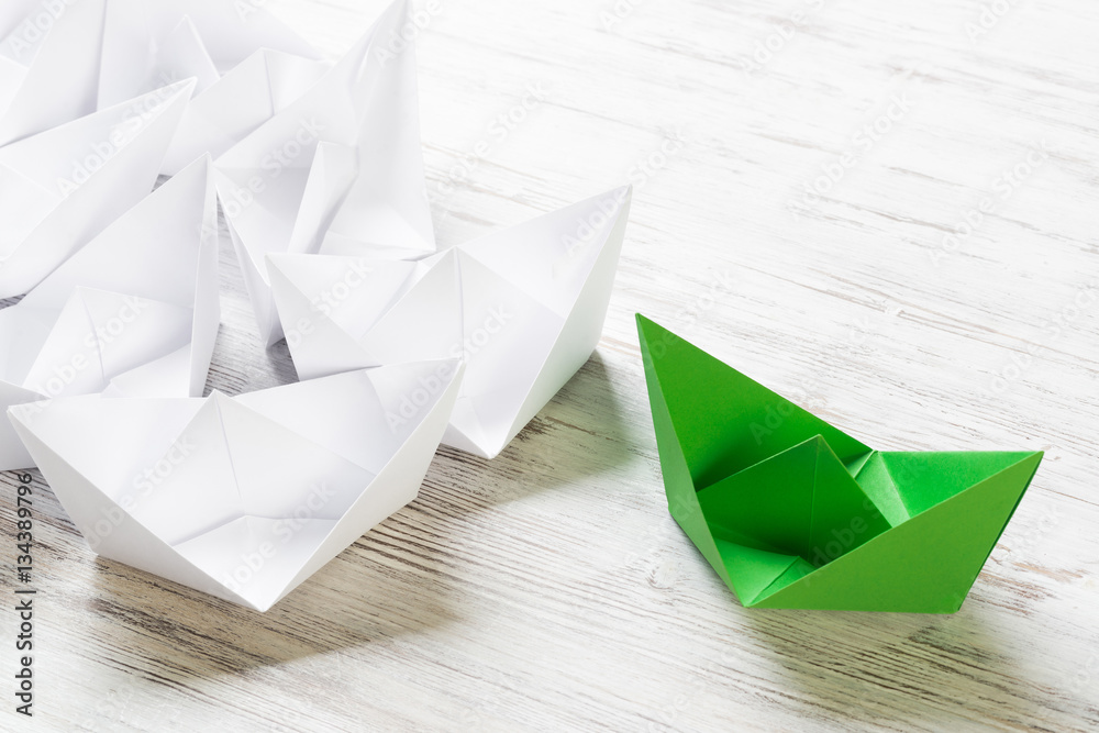 Business leadership concept with white and color paper boats on wooden table