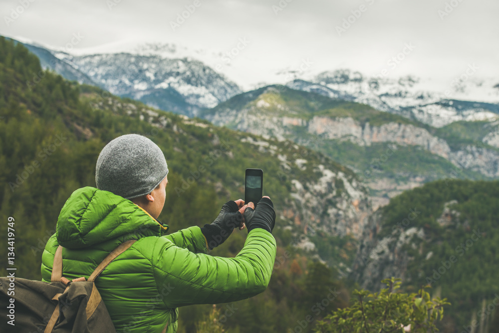 Young man traveller wearing bright clothes making photo of mountains with snowy peaks in Dim Cay dis