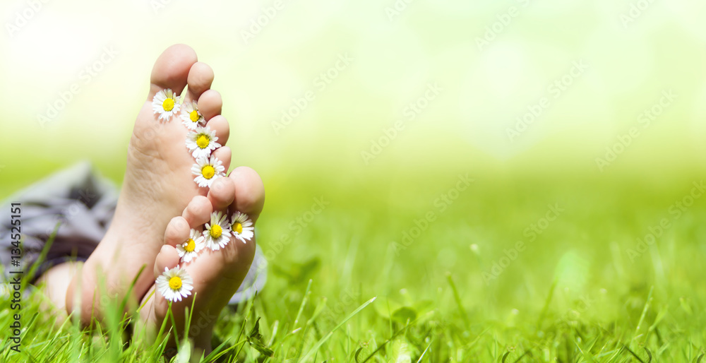 Kinderfüße mit Gänseblümchen auf einer Wiese im Sonnenschein