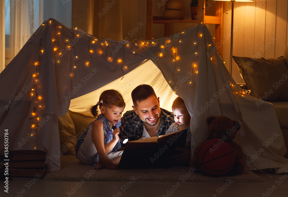 happy family father and children reading a book  in  tent at hom