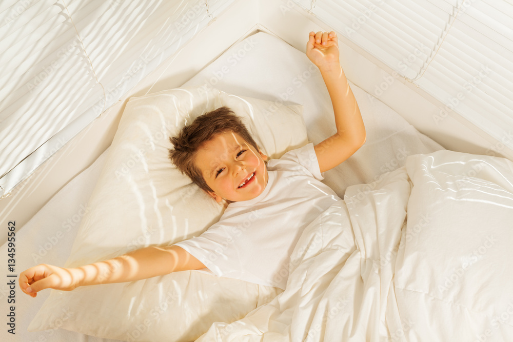 Happy kid boy waking up in his white bedroom