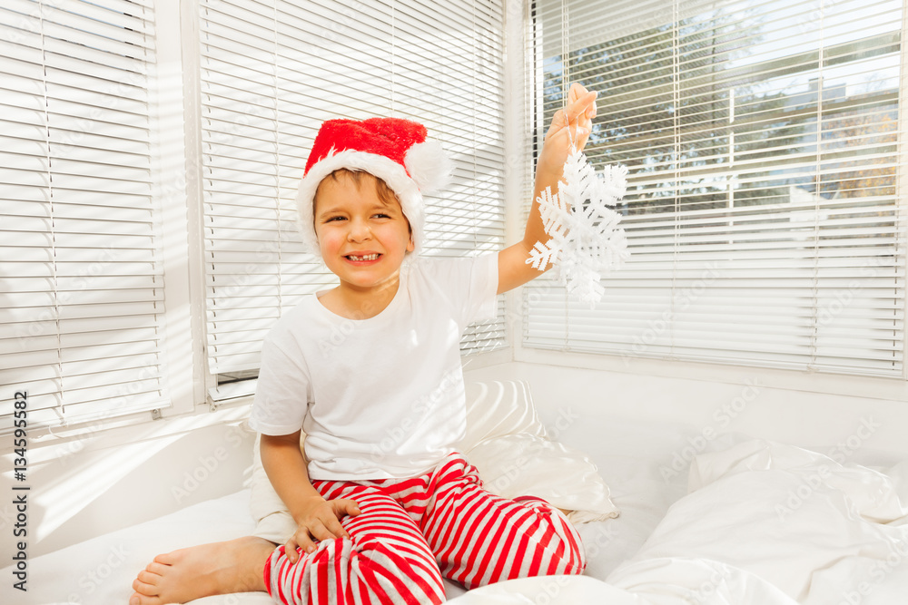 Boy sitting on his bad in pajamas and Santa hat