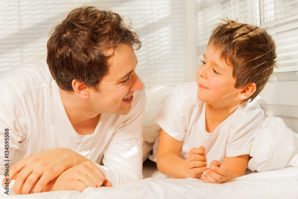 Young dad with his son smiling while lying on bed