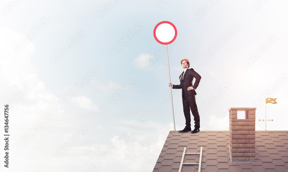 Caucasian businessman on brick house roof showing stop road sign