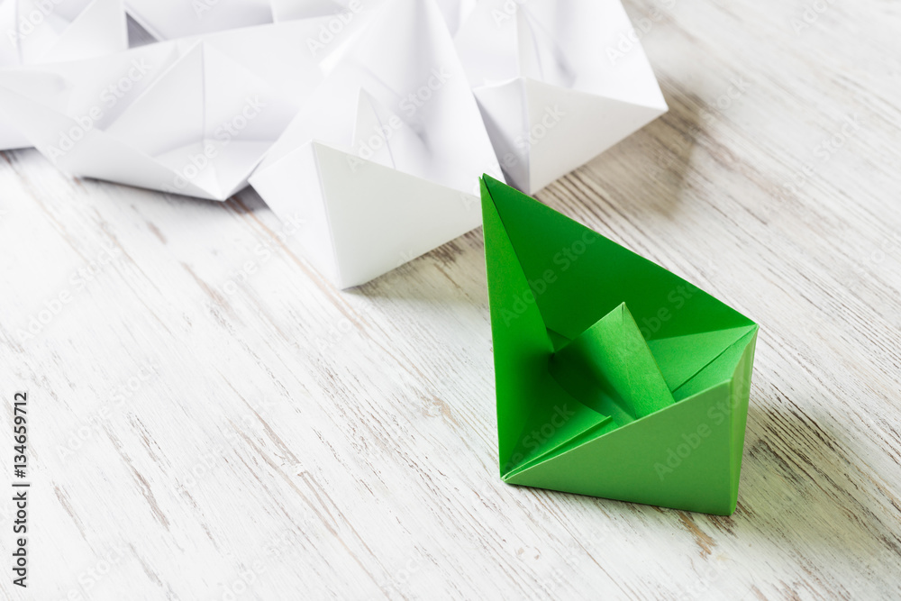 Business leadership concept with white and color paper boats on wooden table