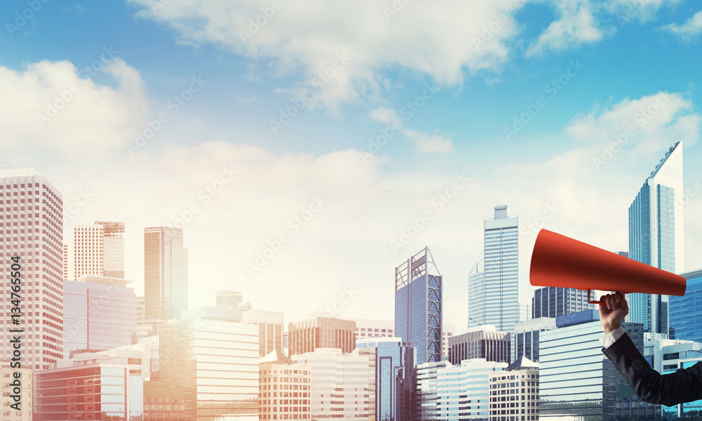 Hand of businesswoman holding red paper trumpet against cityscape background