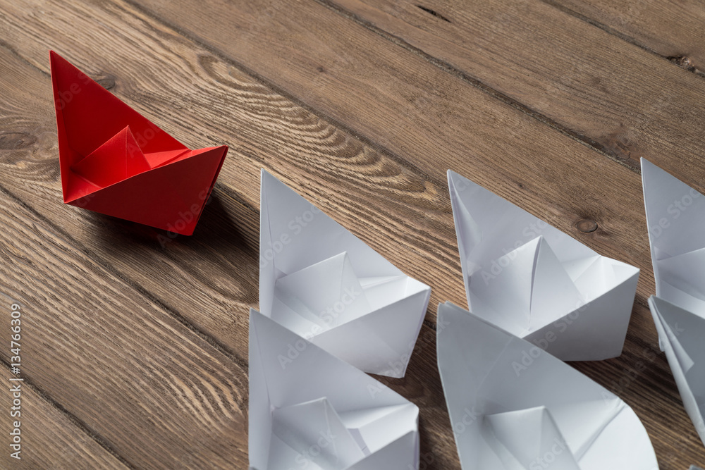 Business leadership concept with white and color paper boats on wooden table