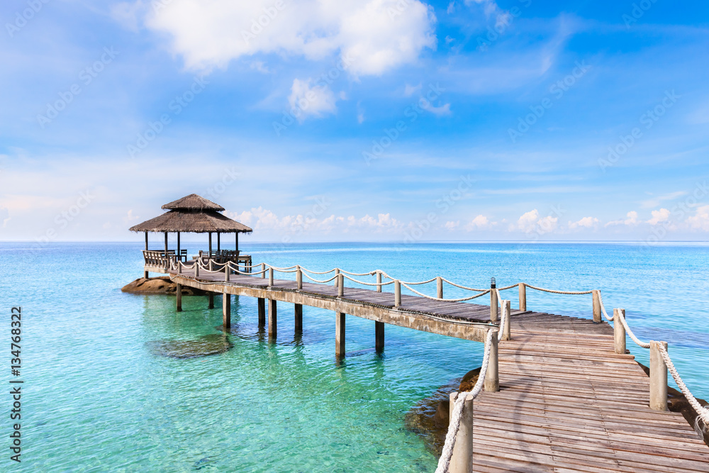 Tropical beach landscape with wooden pier above transparent sea