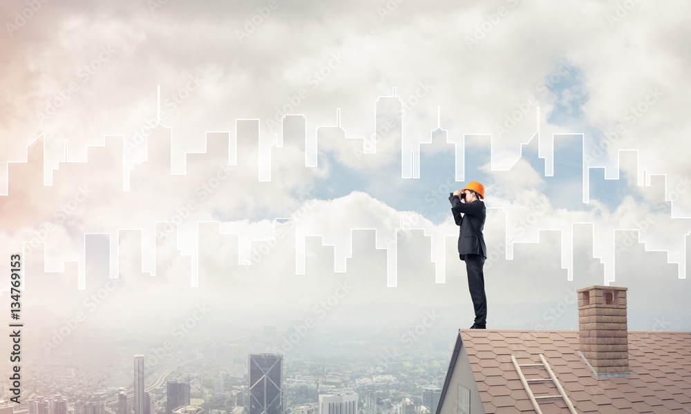 Engineer man standing on roof and looking in binoculars. Mixed m