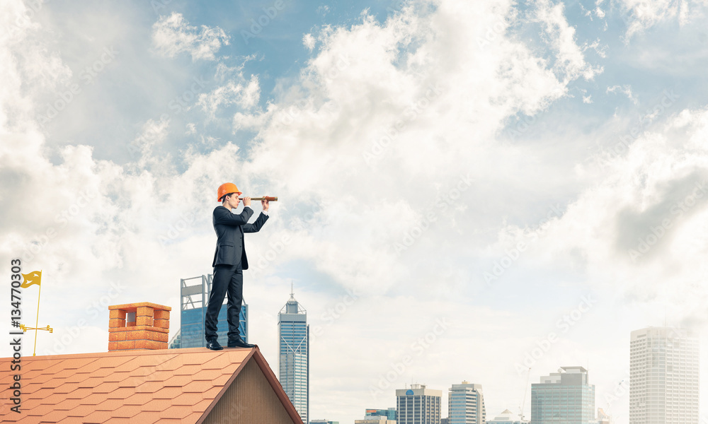 Engineer man standing on roof and looking in spyglass. Mixed med