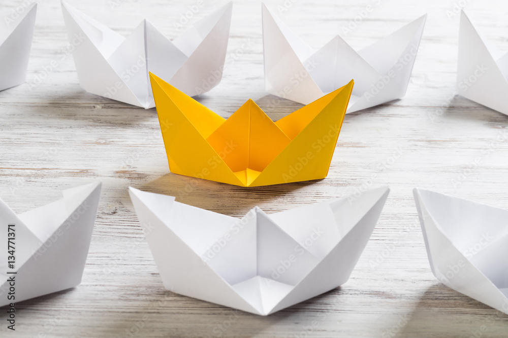 Business leadership concept with white and color paper boats on wooden table