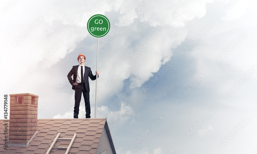 Businessman in suit on house top with ecology concept signboard.