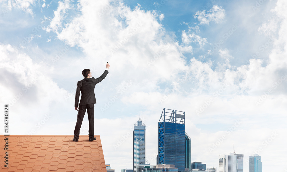 Businessman on house roof touch empty space. Mixed media