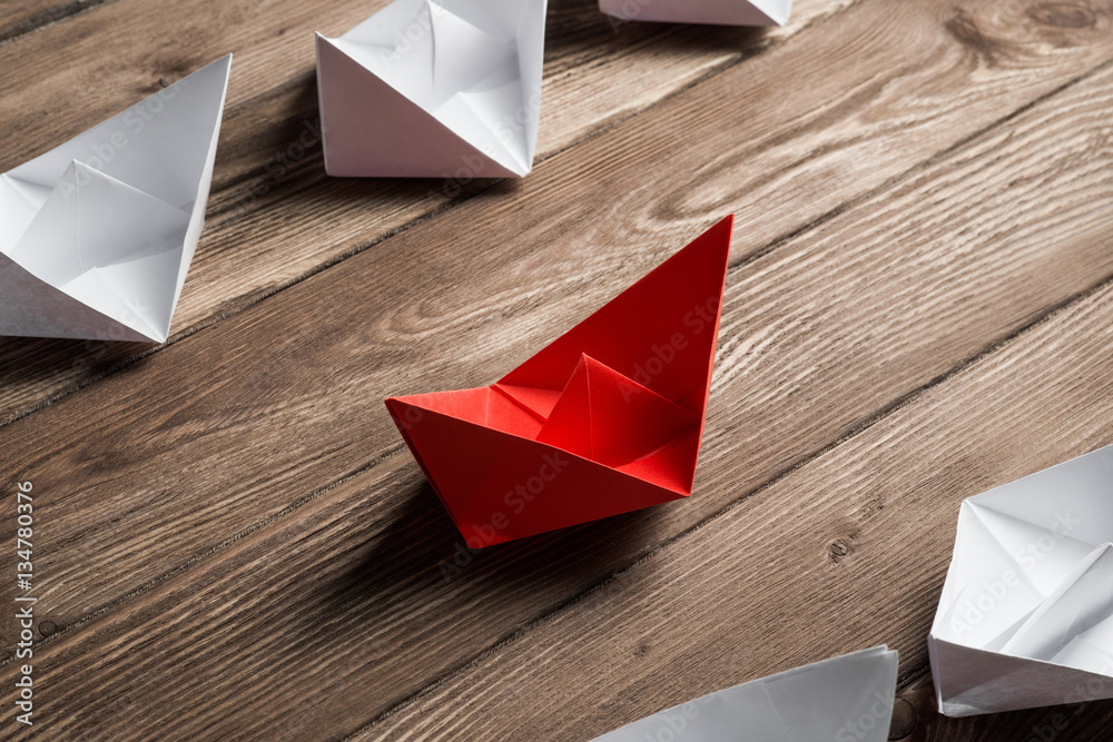 Business leadership concept with white and color paper boats on wooden table