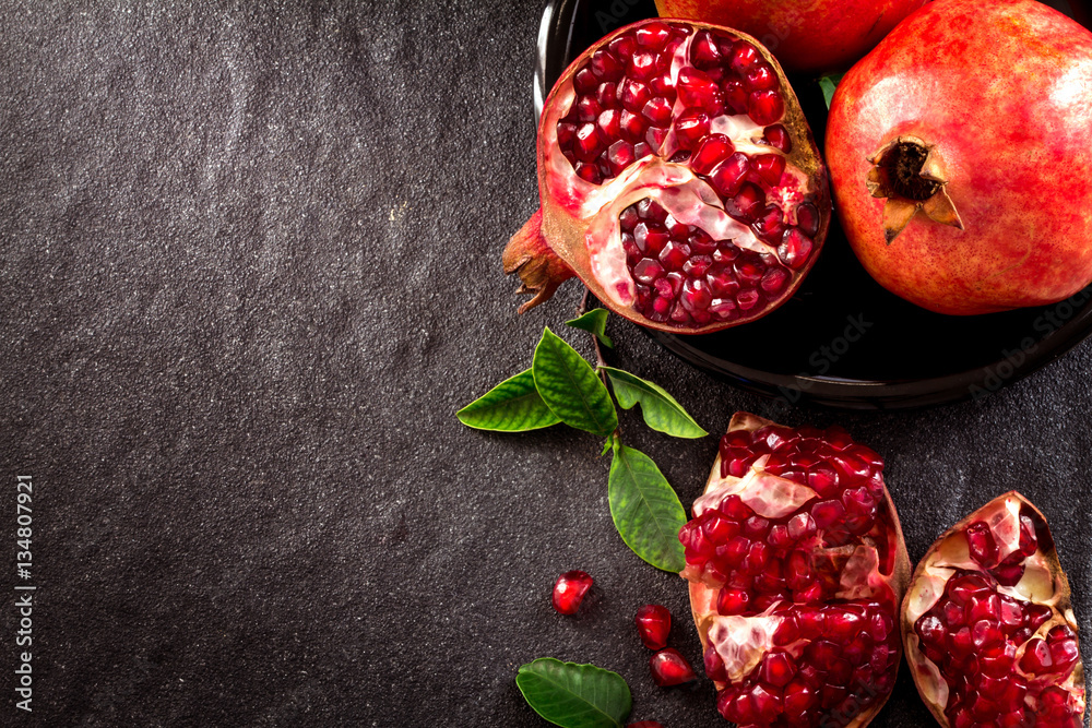 Fresh red pomegranate and seed  with leaves over black stone bac