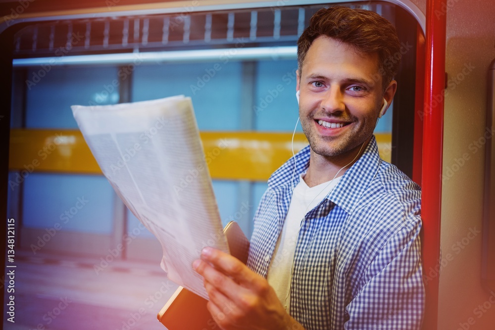 Portrait of handsome man holding newspaper while listening music