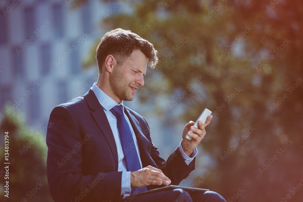 Smiling businessman using mobile phone and digital tablet