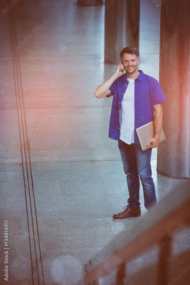 Handsome man holding laptop and talking on mobile phone