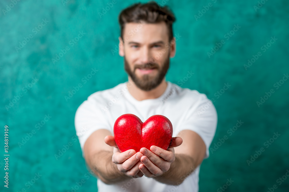 Handsome man in the white t-shirt giving red heart standing on the painted green wall background. im