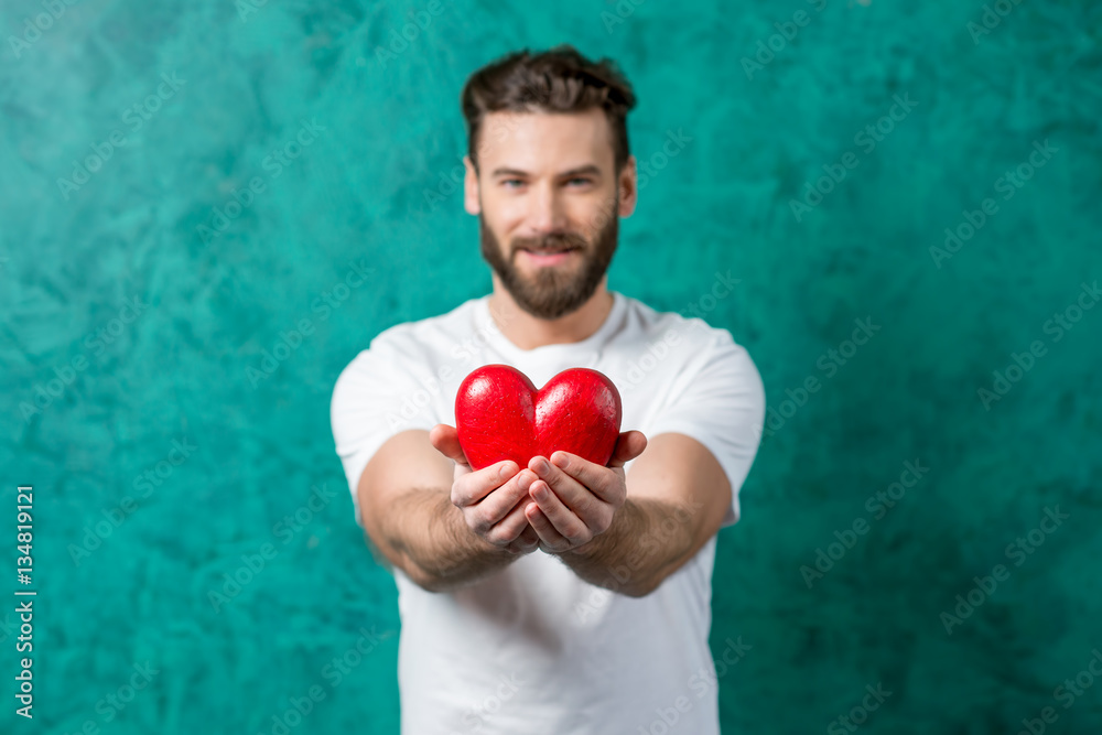 Handsome man in the white t-shirt giving red heart standing on the painted green wall background. im