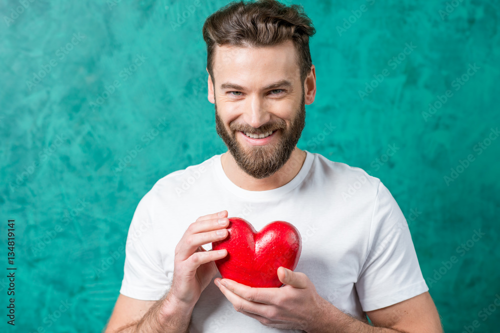 Handsome man in the white t-shirt holding red heart on the painted green wall background. Valentine