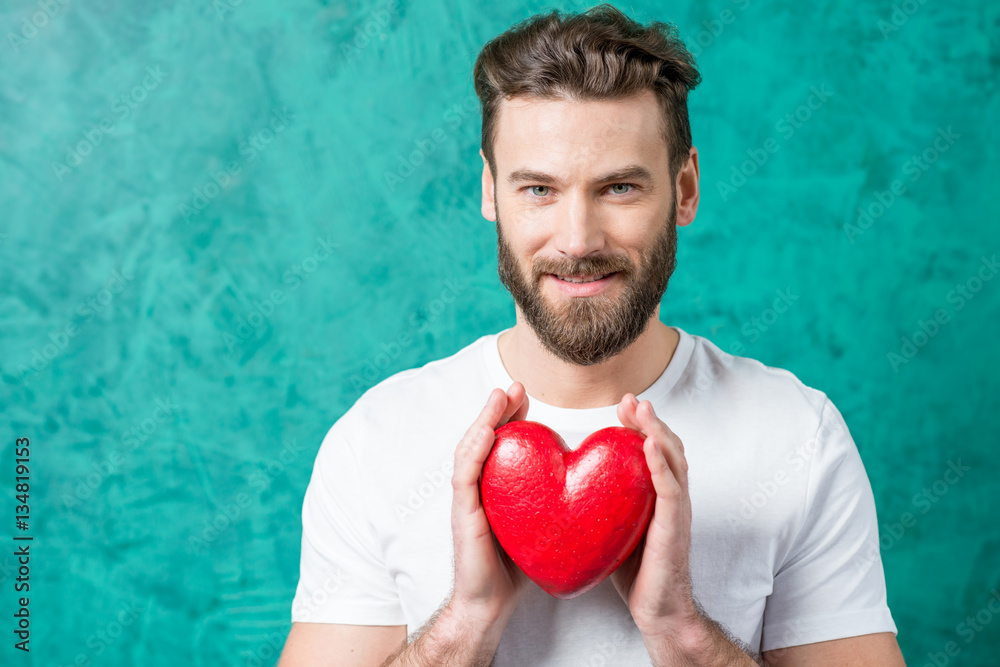 Handsome man in the white t-shirt holding red heart on the painted green wall background. Valentine