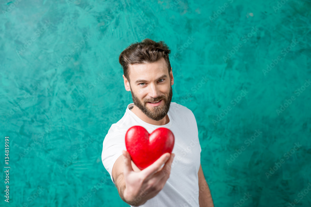 Handsome man in the white t-shirt giving red heart standing on the painted green wall background. Va