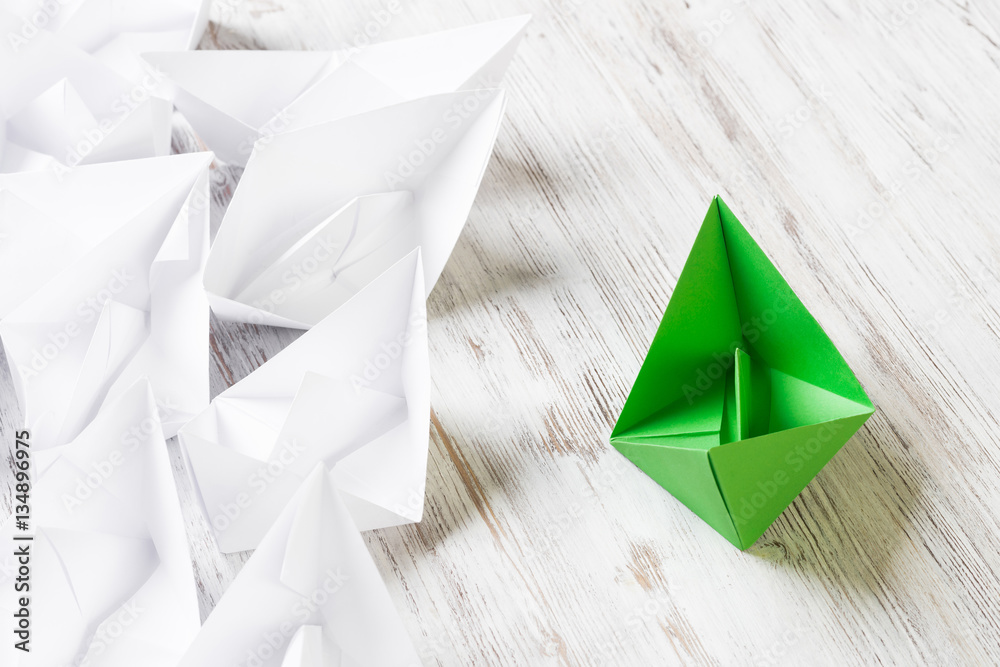 Business leadership concept with white and color paper boats on wooden table