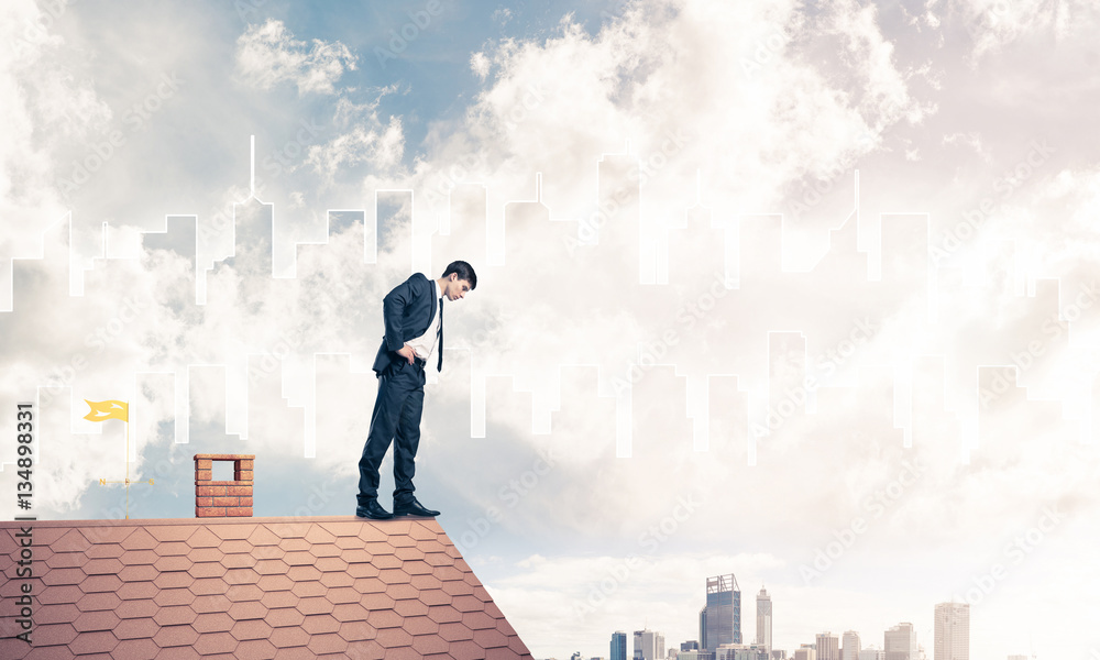 Businessman looking down from roof and modern cityscape at backg